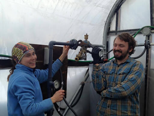 smiling woman next to a man fixing and replacing the broken water heater 